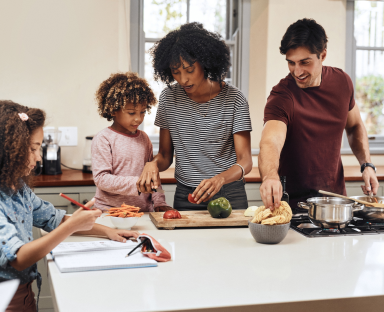 foto di una famiglia: due bambini molto ricci, la mamma nera e il papà bianco, in cucina, mentre cucinano insieme