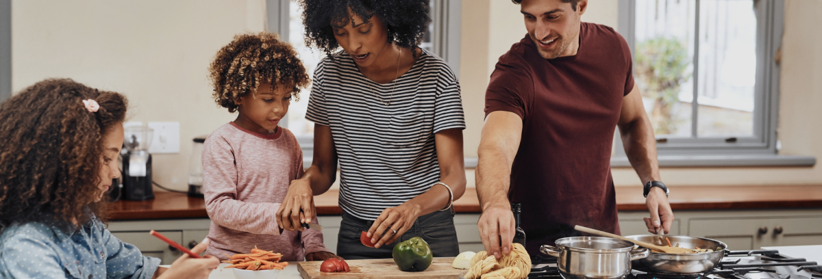 foto di una famiglia: due bambini molto ricci, la mamma nera e il papà bianco, in cucina, mentre cucinano insieme